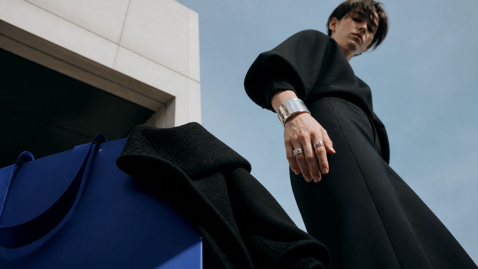 Contre-plongée mode : silhouette en noir et sac bleu cobalt sur fond de ciel